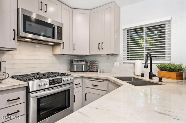 kitchen featuring appliances with stainless steel finishes, white cabinetry, sink, backsplash, and light stone countertops