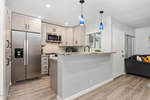 kitchen featuring appliances with stainless steel finishes, pendant lighting, tasteful backsplash, white cabinetry, and light wood-type flooring