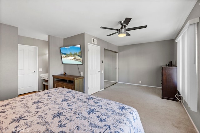 bedroom with ceiling fan, light colored carpet, ensuite bath, and a closet