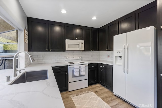 kitchen with light stone countertops, light wood-type flooring, tasteful backsplash, white appliances, and sink