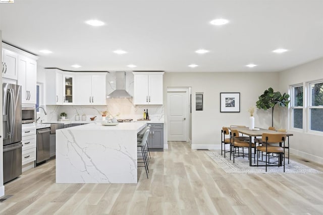 kitchen featuring a center island, white cabinets, stainless steel appliances, and wall chimney range hood