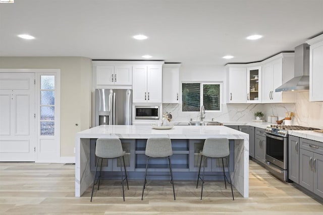 kitchen featuring a center island, stainless steel appliances, gray cabinetry, and wall chimney range hood