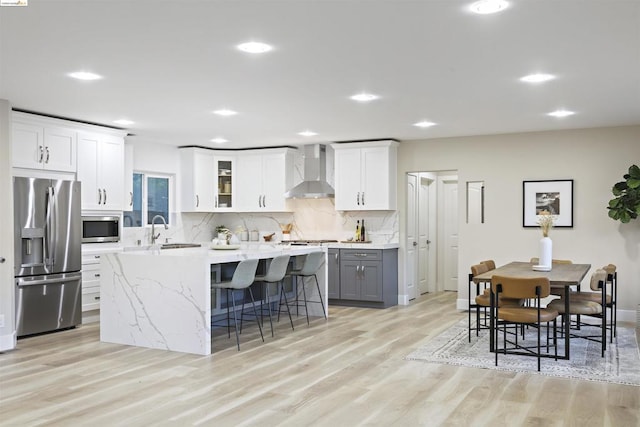 kitchen with gray cabinetry, wall chimney exhaust hood, light wood-type flooring, white cabinetry, and stainless steel appliances