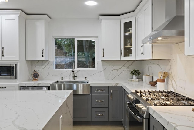 kitchen with wall chimney exhaust hood, stainless steel appliances, backsplash, gray cabinets, and white cabinets