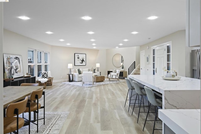 kitchen with a kitchen breakfast bar, light stone countertops, white cabinetry, and light wood-type flooring