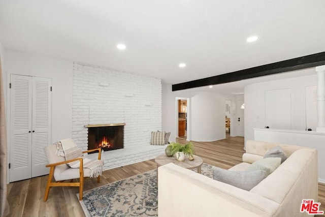 living room with hardwood / wood-style floors, beam ceiling, and a brick fireplace