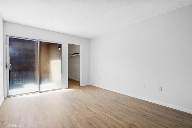 unfurnished bedroom with a spacious closet, a closet, light hardwood / wood-style floors, and a textured ceiling