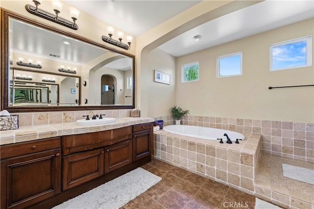 bathroom featuring tile patterned floors, tiled bath, tasteful backsplash, and vanity