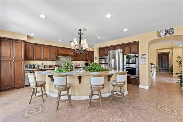 kitchen with pendant lighting, a kitchen breakfast bar, light stone countertops, an island with sink, and appliances with stainless steel finishes