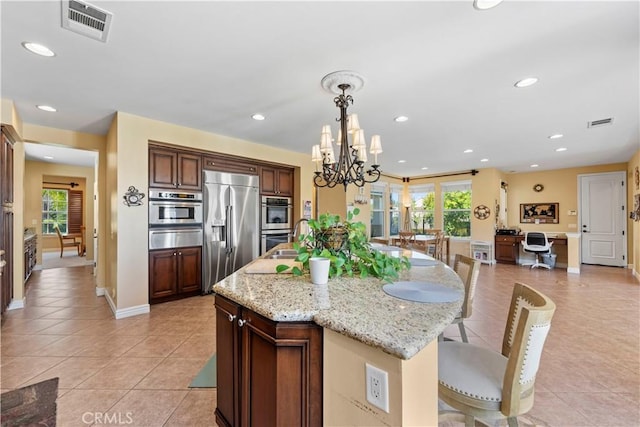 kitchen with light stone countertops, hanging light fixtures, stainless steel appliances, a notable chandelier, and a center island with sink