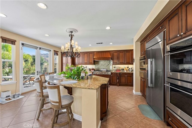 kitchen with light stone counters, light tile patterned floors, hanging light fixtures, and appliances with stainless steel finishes