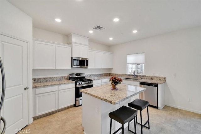 kitchen with appliances with stainless steel finishes, light stone counters, a breakfast bar, white cabinets, and a kitchen island