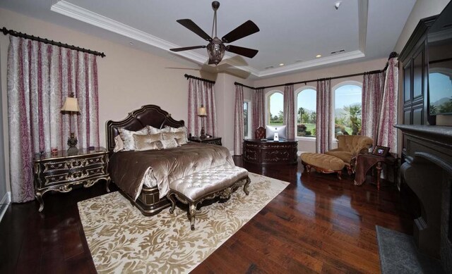 bedroom featuring a tray ceiling, crown molding, ceiling fan, and dark wood-type flooring