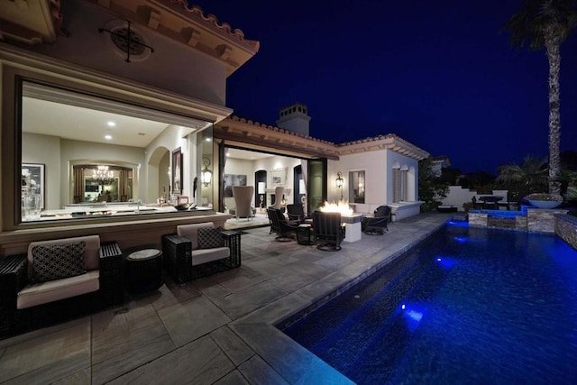 pool at night featuring a jacuzzi, a patio, pool water feature, and an outdoor living space with a fire pit