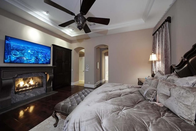 bedroom with ceiling fan, dark hardwood / wood-style floors, crown molding, a tray ceiling, and a fireplace