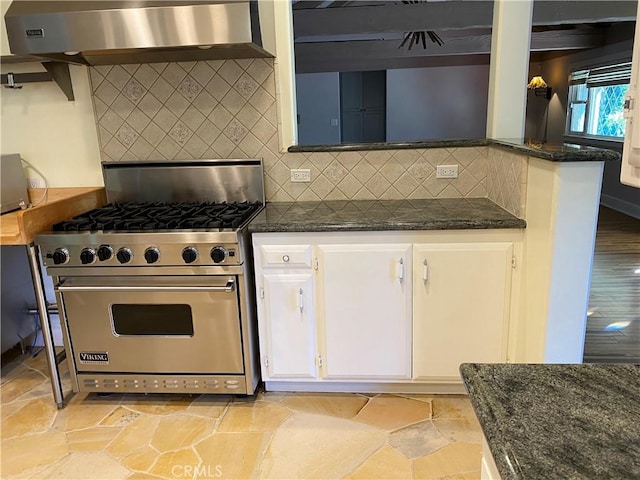 kitchen featuring white cabinetry, wall chimney range hood, backsplash, dark stone countertops, and premium stove