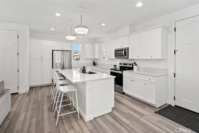 kitchen featuring a kitchen island with sink, white cabinets, light wood-type flooring, and appliances with stainless steel finishes