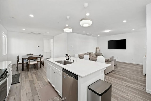 kitchen with stainless steel appliances, sink, light hardwood / wood-style floors, white cabinetry, and an island with sink