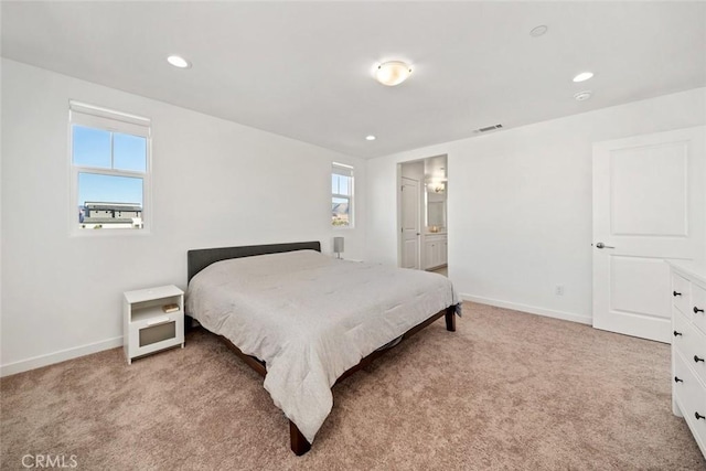 bedroom featuring connected bathroom, multiple windows, and light colored carpet