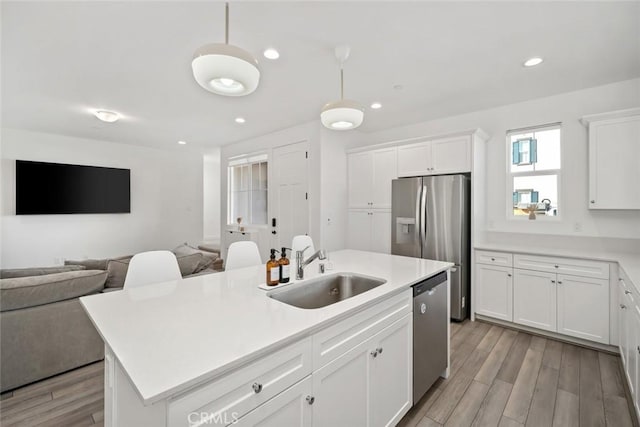 kitchen with pendant lighting, sink, light wood-type flooring, an island with sink, and appliances with stainless steel finishes