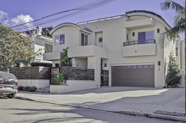 art deco home with an attached garage, a balcony, fence, concrete driveway, and stucco siding