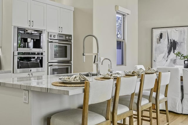 kitchen with double oven, a breakfast bar, light wood finished floors, and light stone counters