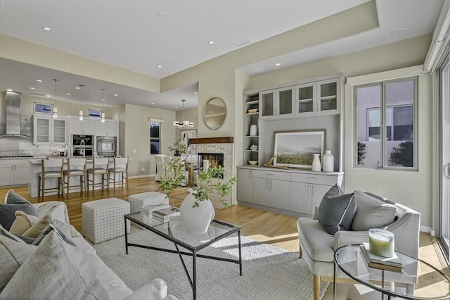 living room with built in shelves, light wood finished floors, recessed lighting, a stone fireplace, and baseboards