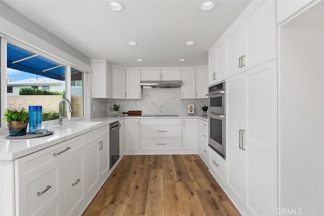 kitchen featuring white cabinetry, sink, stainless steel double oven, tasteful backsplash, and light wood-type flooring