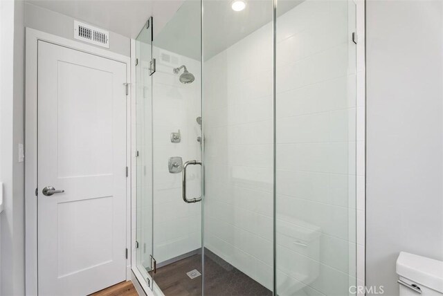 bathroom with toilet, a shower with shower door, and hardwood / wood-style flooring