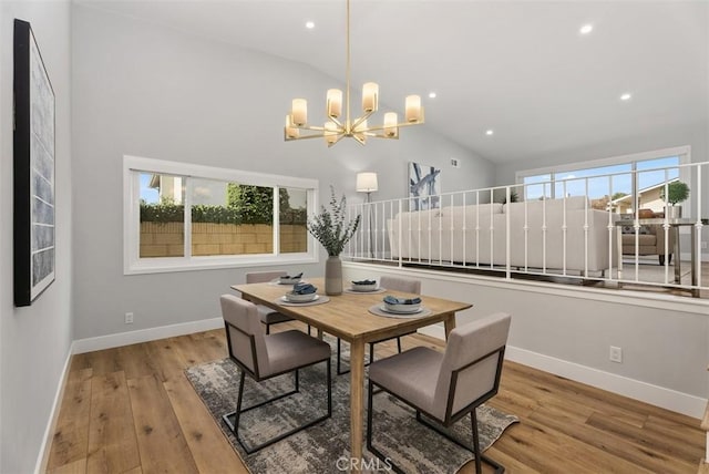 dining room with a healthy amount of sunlight, light hardwood / wood-style floors, high vaulted ceiling, and an inviting chandelier