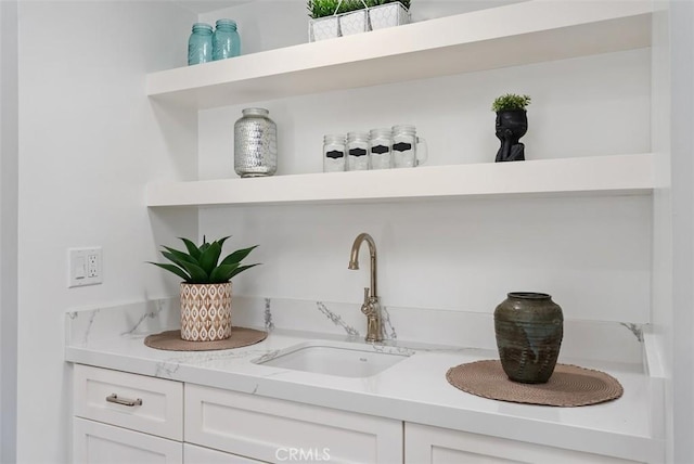 bar with white cabinets, light stone countertops, and sink