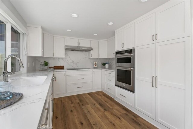 kitchen featuring white cabinetry, sink, stainless steel double oven, light stone counters, and dark hardwood / wood-style flooring