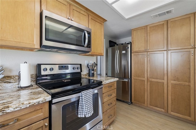 kitchen with light stone countertops, appliances with stainless steel finishes, and light hardwood / wood-style flooring