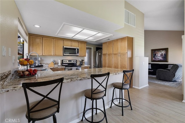 kitchen featuring light hardwood / wood-style flooring, kitchen peninsula, vaulted ceiling, a breakfast bar area, and appliances with stainless steel finishes