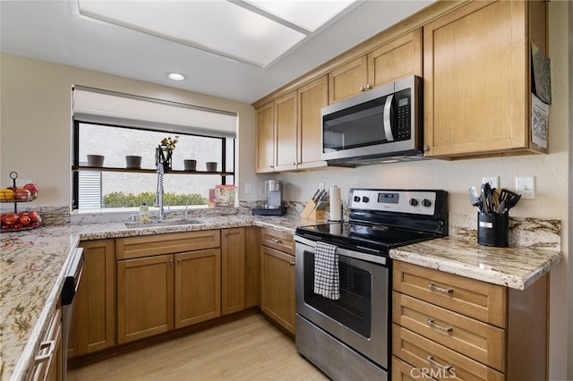 kitchen with light stone counters, sink, appliances with stainless steel finishes, and light hardwood / wood-style flooring