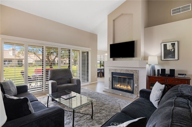 living room with a high end fireplace, light hardwood / wood-style floors, and high vaulted ceiling