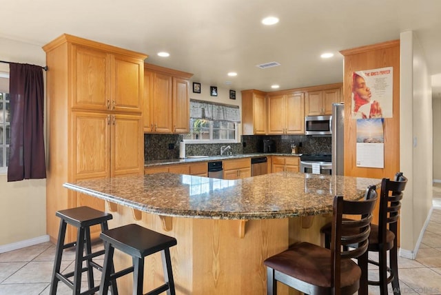 kitchen with dark stone counters, a center island, light tile patterned floors, and stainless steel appliances