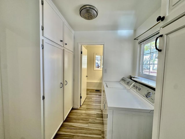 clothes washing area featuring light hardwood / wood-style floors, cabinets, and washing machine and clothes dryer