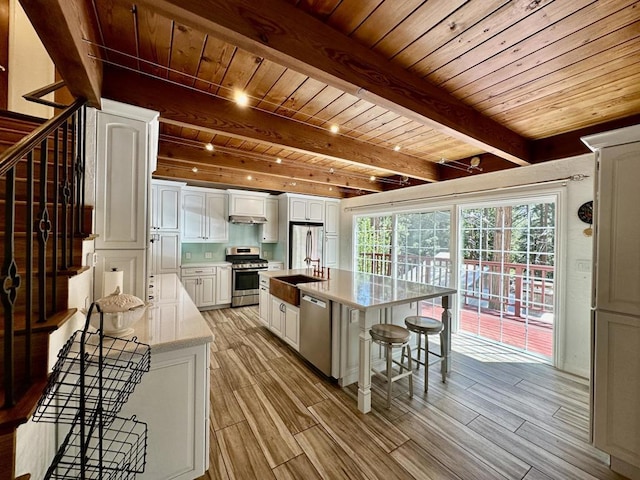 kitchen with white cabinets, a center island with sink, wooden ceiling, and appliances with stainless steel finishes