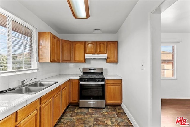 kitchen featuring tile countertops, decorative backsplash, sink, and stainless steel gas range