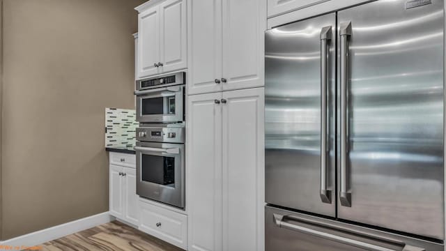 kitchen featuring white cabinets, light hardwood / wood-style floors, backsplash, and appliances with stainless steel finishes