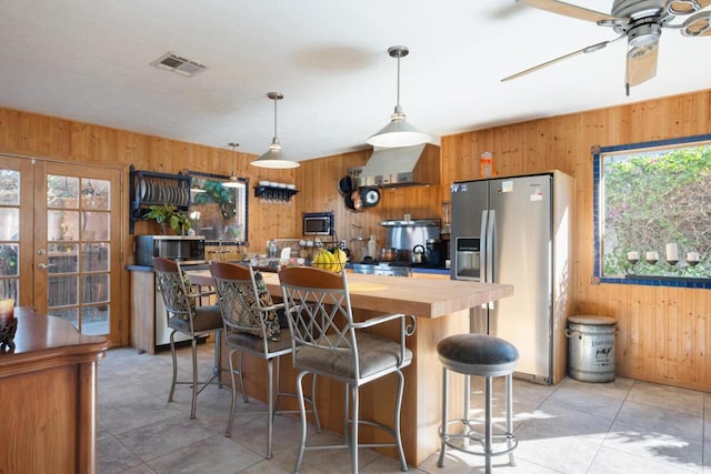 kitchen with hanging light fixtures, wall chimney exhaust hood, a breakfast bar area, and stainless steel appliances