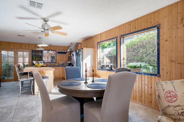 tiled dining room featuring french doors, ceiling fan, and wood walls