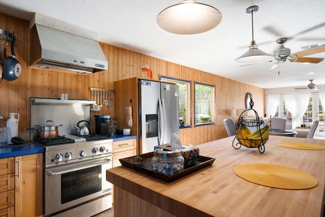 kitchen featuring appliances with stainless steel finishes, wood counters, wall chimney range hood, plenty of natural light, and wood walls