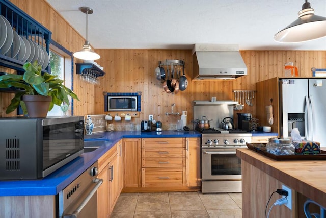 kitchen featuring wall chimney range hood, light tile patterned floors, stainless steel appliances, and wooden walls