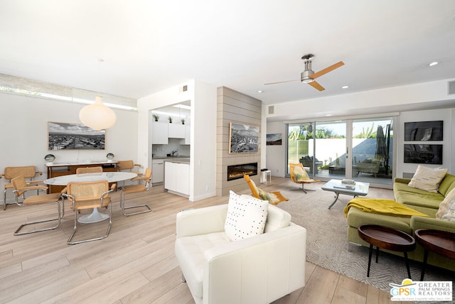 living room featuring a fireplace, light wood-type flooring, and ceiling fan