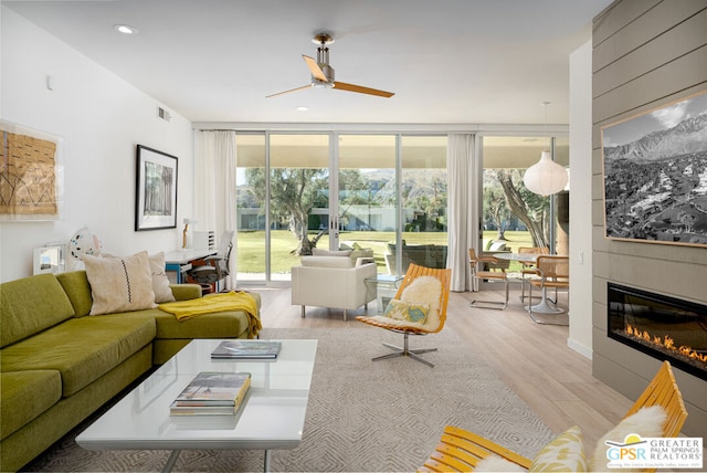 living room featuring plenty of natural light, ceiling fan, a fireplace, and light hardwood / wood-style flooring