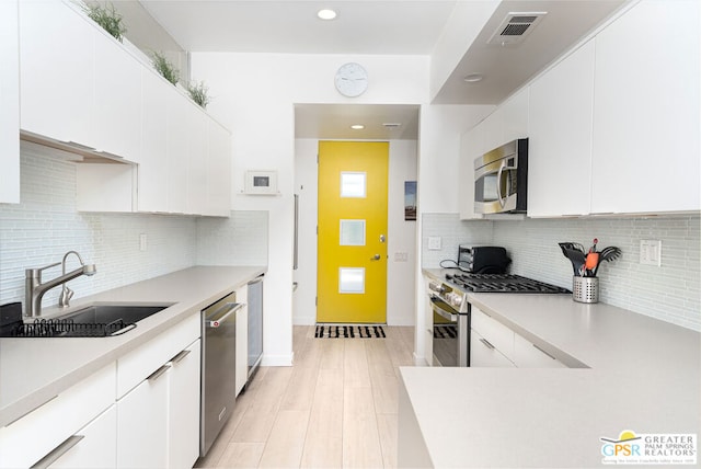 kitchen with backsplash, stainless steel appliances, sink, light hardwood / wood-style flooring, and white cabinetry