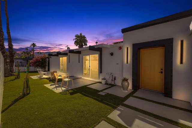 back house at dusk featuring a patio area and a yard