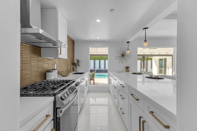 kitchen with wall chimney range hood, white cabinetry, hanging light fixtures, tasteful backsplash, and gas stove